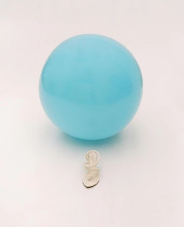 Close-up shot of a single white strappy sandal placed beneath a light-blue balloon, set against a clean, bright white backdrop.