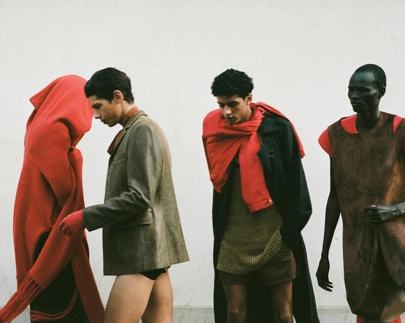 Fashion editorial shot of four men in a line wearing stylish outfits, set against a plain white background, showcasing modern clothing design.
