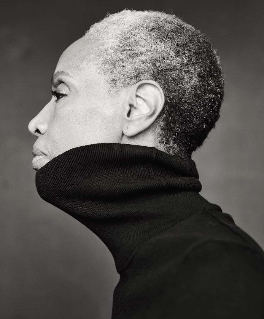 Profile portrait of an adult woman with short, grey hair wearing a black turtleneck sweater against a dark grey backdrop.