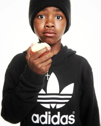 Young child in a black beanie and black hoodie eating an apple against a plain white background