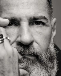 Close-up monochrome portrait of an older man with a full beard and rings on his fingers by photographer Daymion Mardel