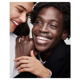 Close-up portrait of a smiling Black man and a smiling white woman wearing gold rings against a white seamless background
