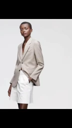 Model wearing a neutral beige blazer and white tailored shorts against a plain white background by Daymion Mardel.