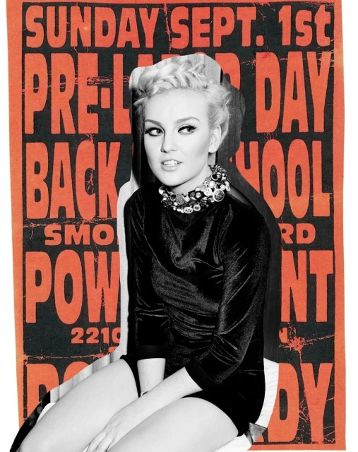 A fair-skinned woman with blonde hair wears a black velvet dress and jeweled collar necklace in front of an orange graphic poster.