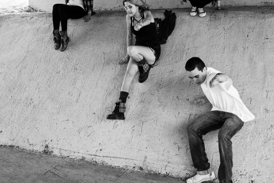 Monochrome image of three young adults on a concrete structure, one climbing down, showcasing casual wear and urban setting in black and white.