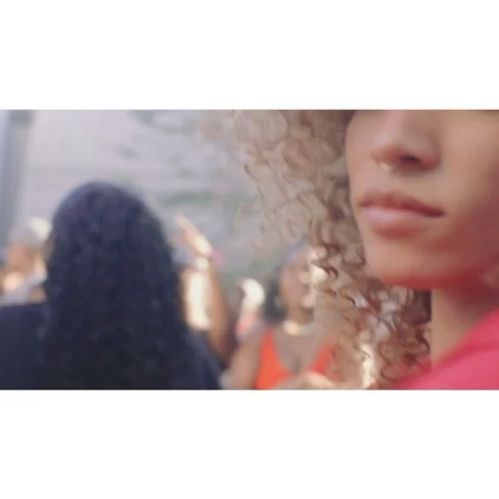 Close-up of an adult female with curly blonde hair and a nose ring, with a blurred crowd in the background at an outdoor event.