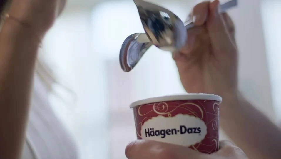 Close up of a woman holding a cup of Haagen-Dazs ice cream while scooping ice cream with a spoon, capturing a moment of indulgence.