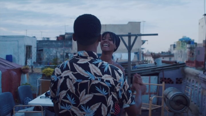 A cheerful couple embraces on a rooftop, set against a backdrop of urban buildings and a cloudy sky, capturing a moment of joy and connection.