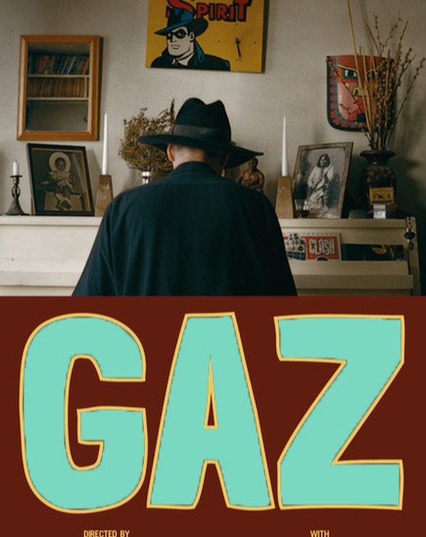 Man at a piano with comic book and framed pictures on the wall above. 'Gaz' title text in turquoise and yellow below image.