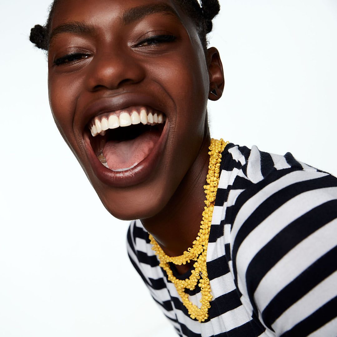 Close-up of a laughing African-American woman wearing a black and white striped shirt and a yellow beaded necklace against a white background.