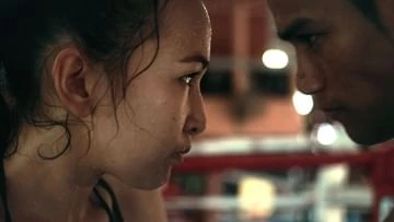 Close-up portrait of two Asian adults facing each other, with a boxing ring and blurred background, intense mood, and dramatic lighting.