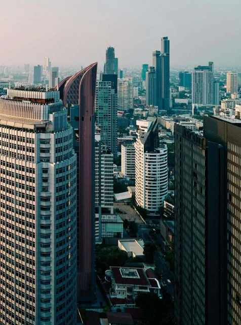 High-angle cityscape featuring many high-rise buildings and skyscrapers, forming a dense urban environment against a hazy sky.