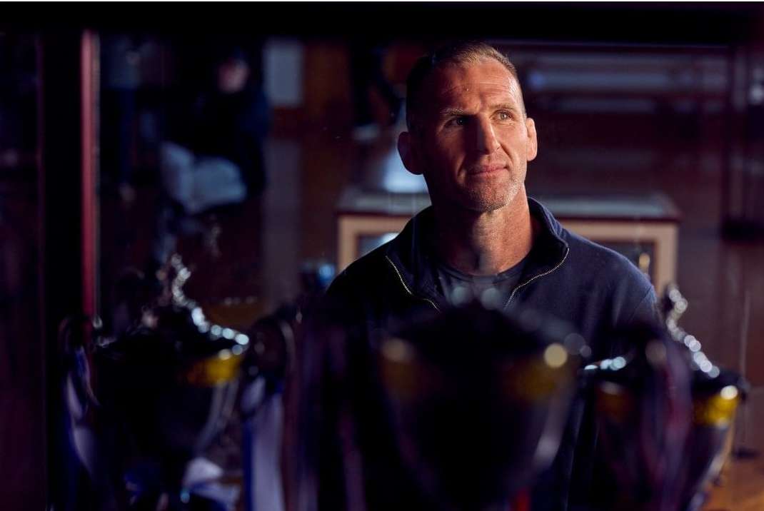 Portrait of an adult male looking off camera in front of a trophy collection, captured with natural lighting in an indoor environment.
