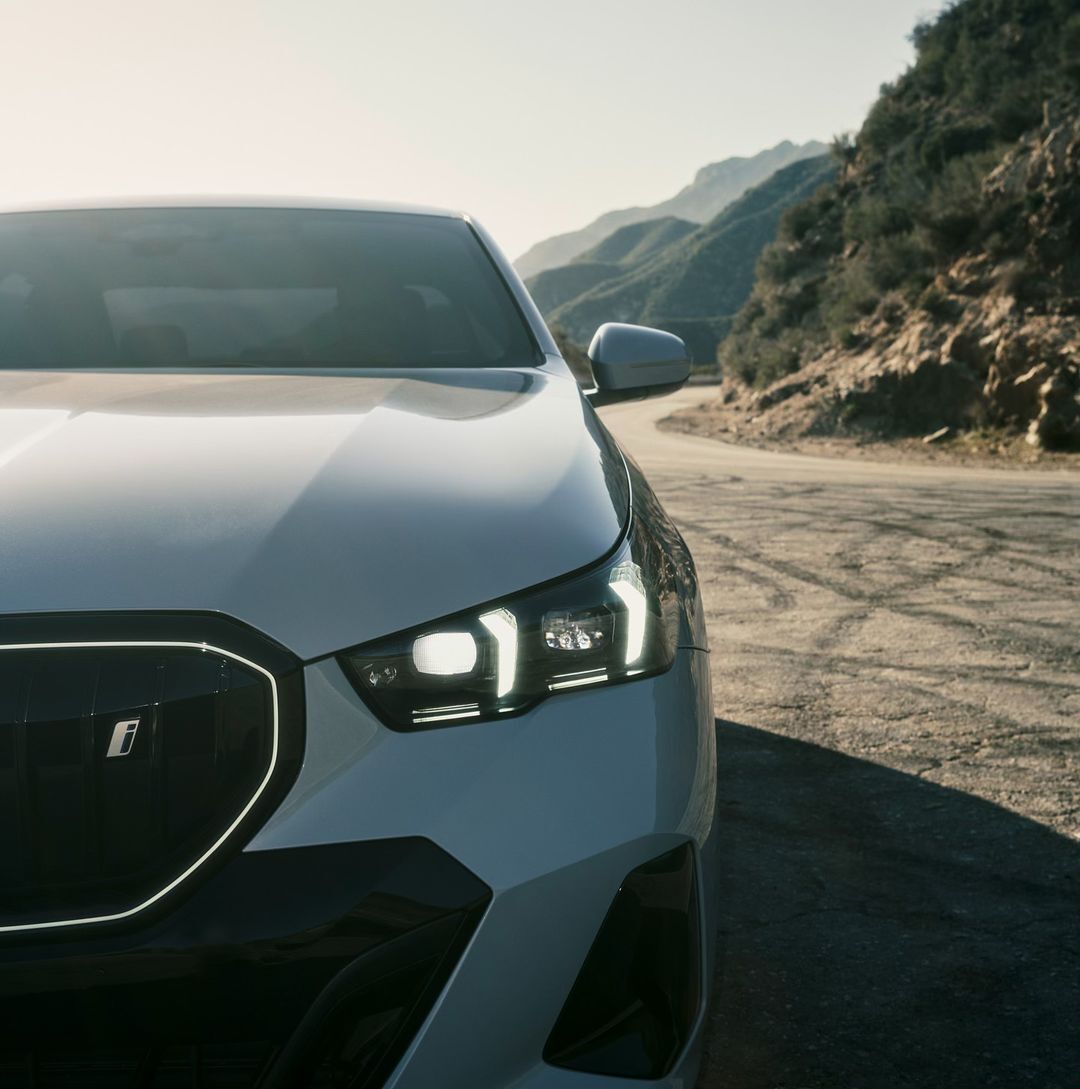 Close-up of a white crossover SUV parked on a winding road, with mountains in the background on a sunny day, highlighting automotive design.