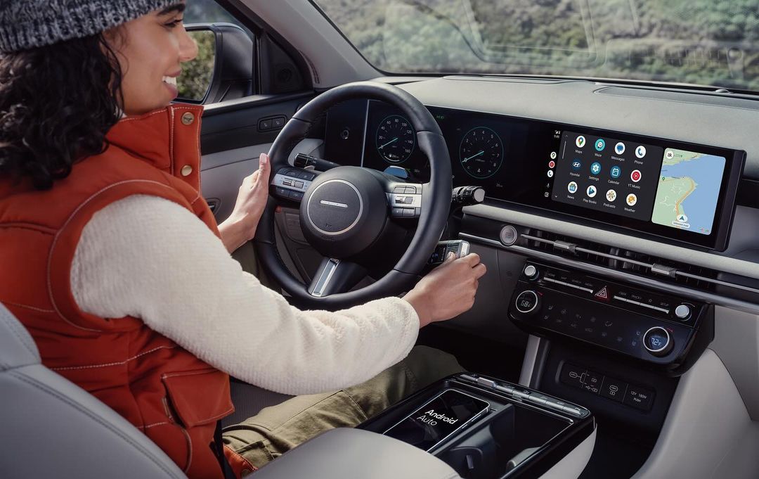 Woman driving a modern car with a digital dashboard display showing navigation and apps, interior view.