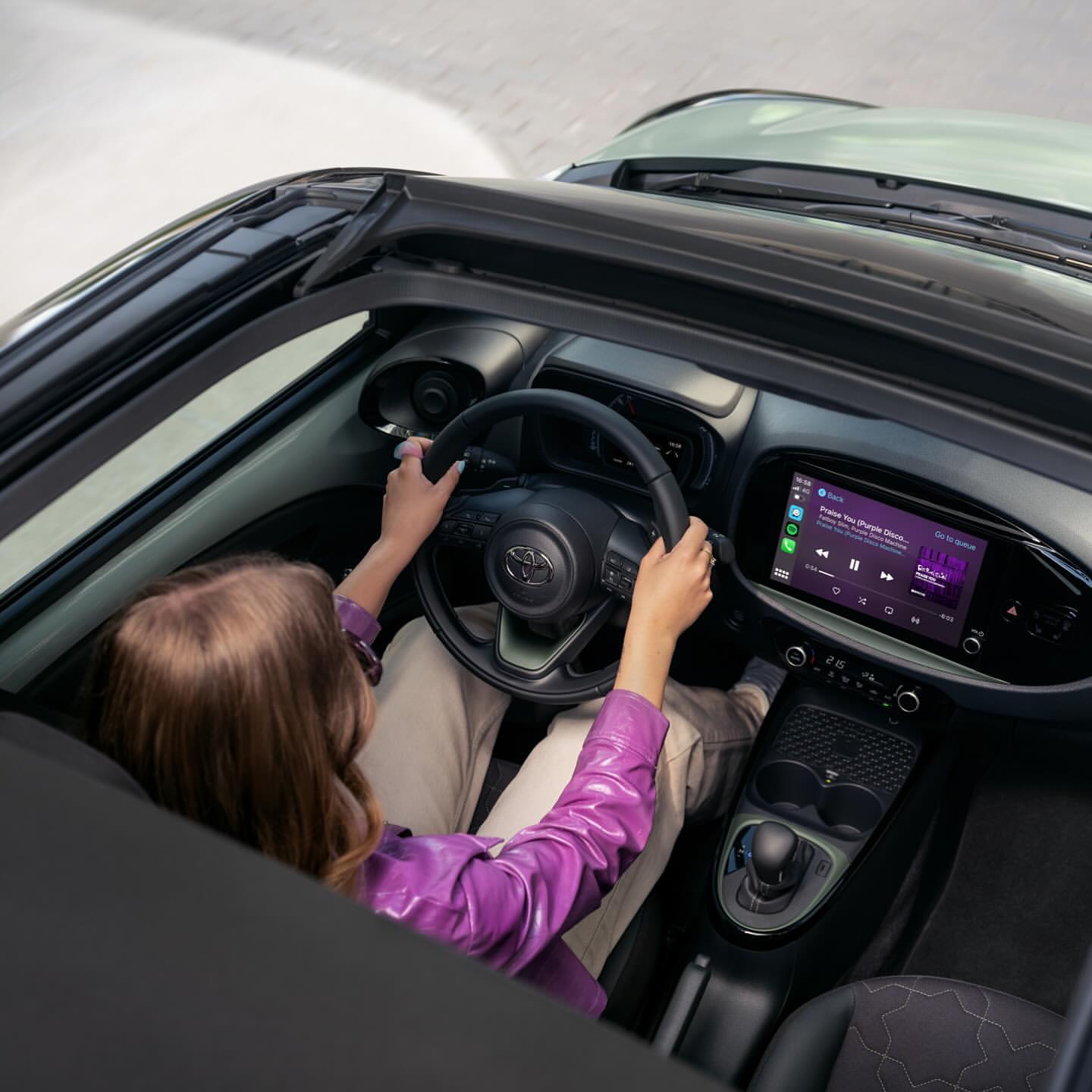 Overhead shot of a woman driving a car with the top down, showcasing the dashboard, interior, and a glimpse of the outside.
