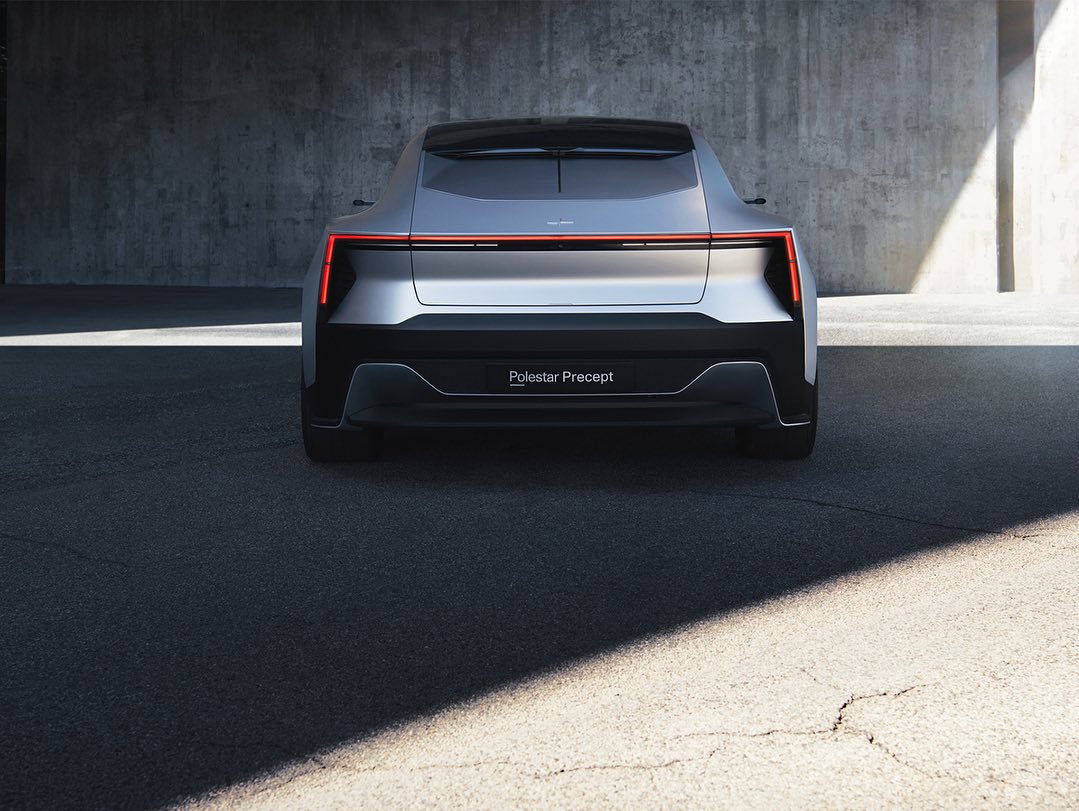 Rear view of a silver Polestar Precept car against a concrete wall on an asphalt surface, capturing its sleek design and modern aesthetic.