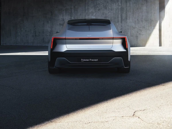 Rear view of a silver Polestar Precept car against a concrete wall on an asphalt surface, capturing its sleek design and modern aesthetic.