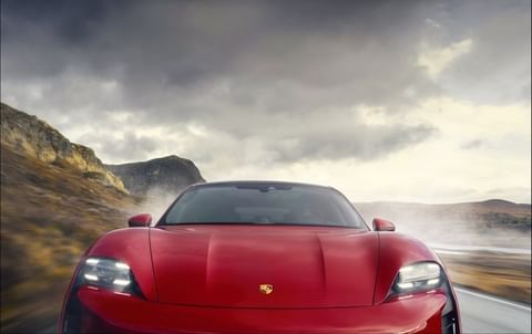 Red Porsche Taycan on a scenic open road with dramatic cloudy skies and rocky hills in the background. Automotive design, landscape.