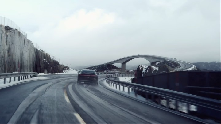 An automotive shot shows a sedan driving on a snow-covered road toward a bridge, emphasizing winter driving conditions and vehicle design.
