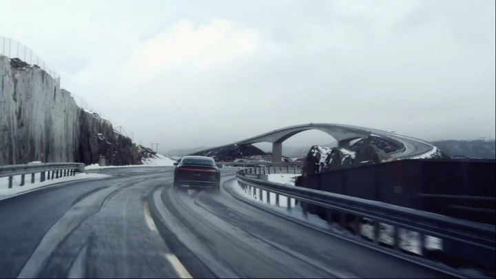 An automotive shot shows a sedan driving on a snow-covered road toward a bridge, emphasizing winter driving conditions and vehicle design.