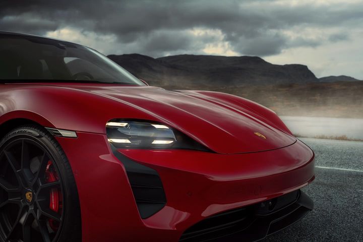 Close-up of a red Porsche Taycan showcasing its sleek design, headlights, and wheel against a backdrop of moody skies and mountains.