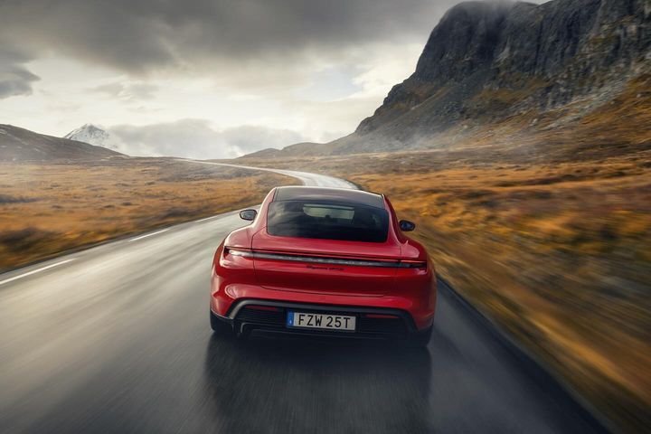 Red Polestar sports car driving on a winding road through a mountainous landscape under a cloudy sky, captured from a rear view.