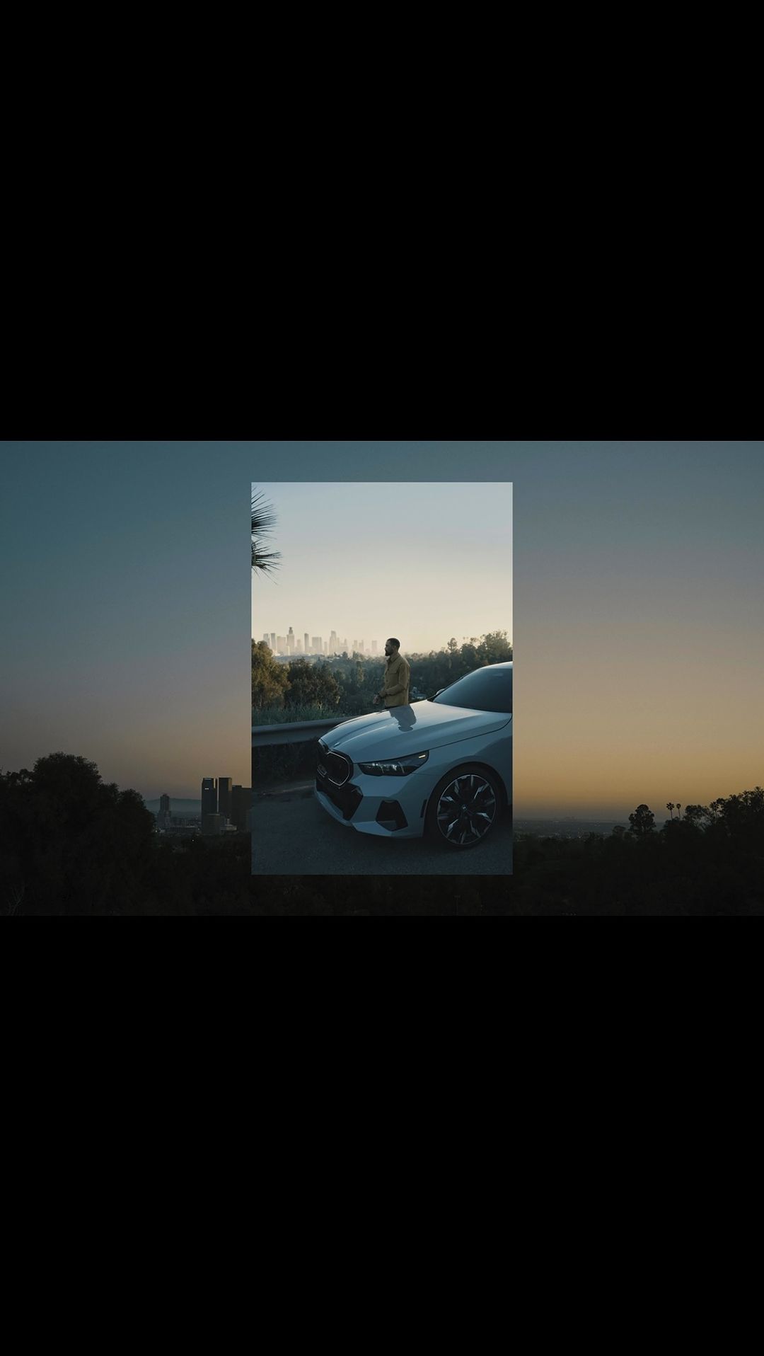 A stylish male model poses on the hood of a white BMW with a cityscape view at dusk, showcasing automotive elegance and urban lifestyle.