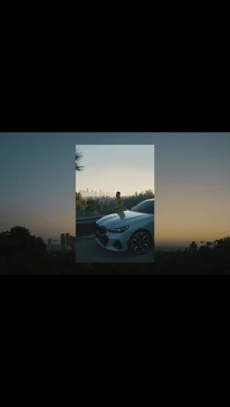 A stylish male model poses on the hood of a white BMW with a cityscape view at dusk, showcasing automotive elegance and urban lifestyle.