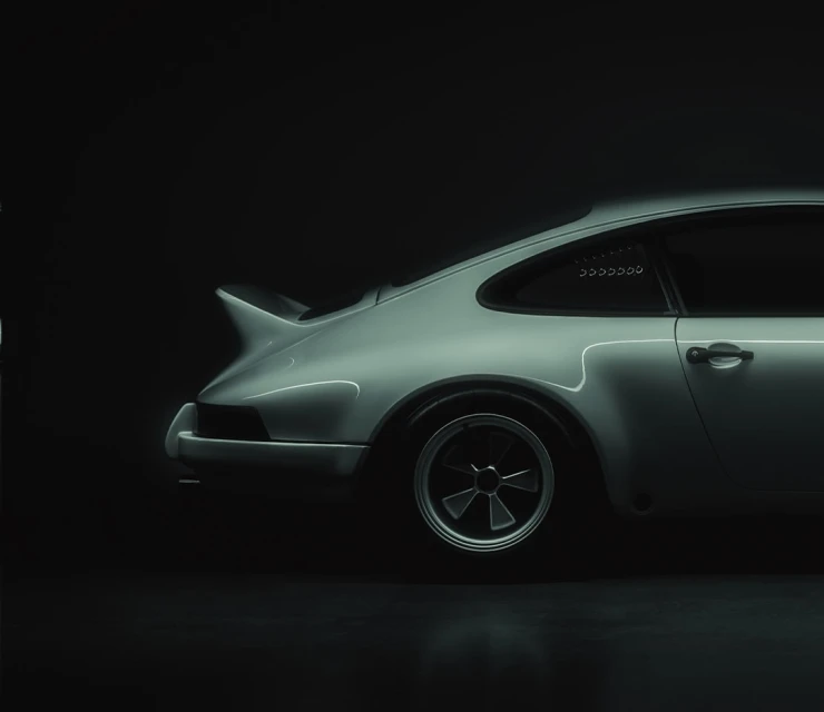 Sleek, side-view studio shot of a vintage silver sports car with black wheels, set against a deep, dark backdrop for automotive advertising.