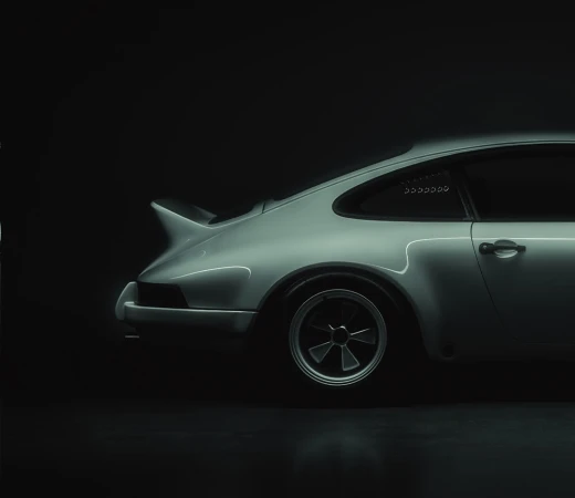 Sleek, side-view studio shot of a vintage silver sports car with black wheels, set against a deep, dark backdrop for automotive advertising.