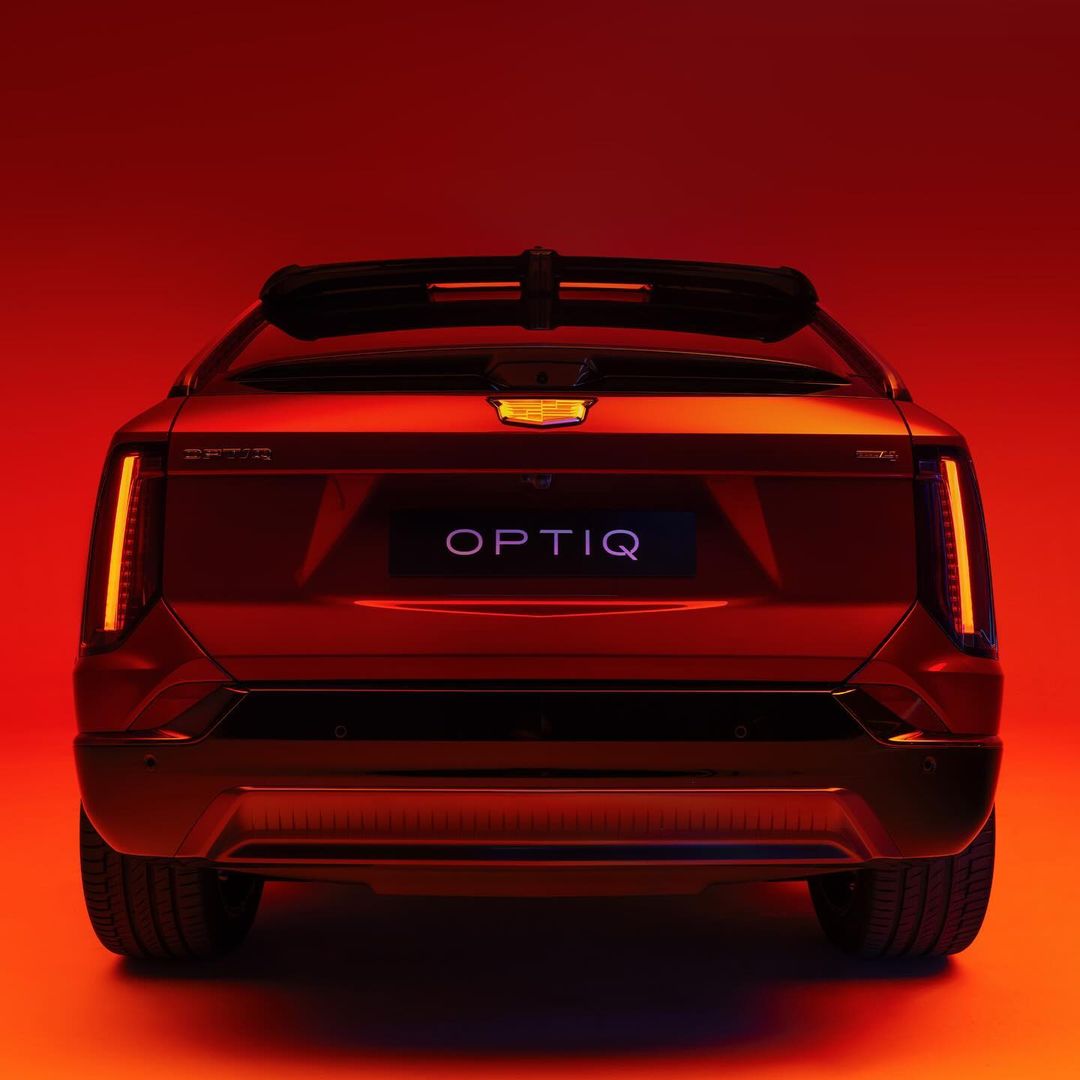 Rear view of a Cadillac Optiq electric vehicle in a studio setting with dramatic red lighting and visible tire detail.