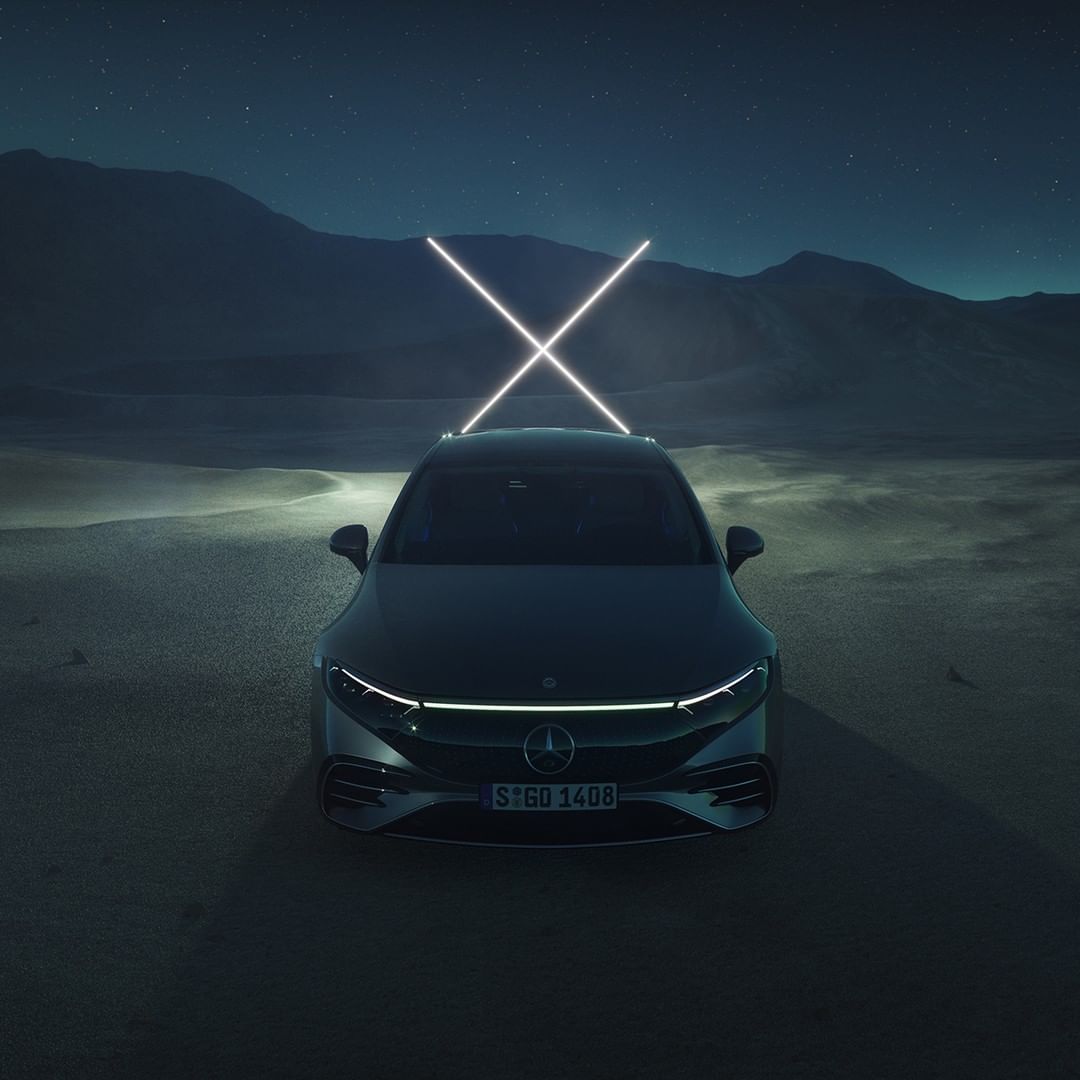 Front view of a dark grey Mercedes-Benz SUV in a desert setting at night, featuring crossed neon lights above the vehicle.