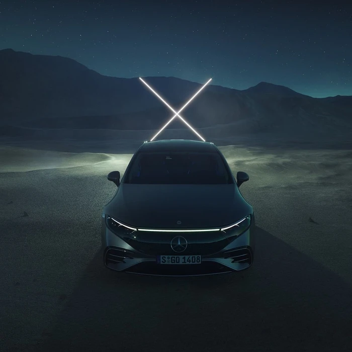 Front view of a dark luxury electric car parked in a desert landscape under a starry night sky with glowing light sticks mounted on the roof.