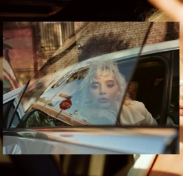 Blonde woman looking through a car window reflecting a stop sign and brick building, photographed by Dejan and Per.