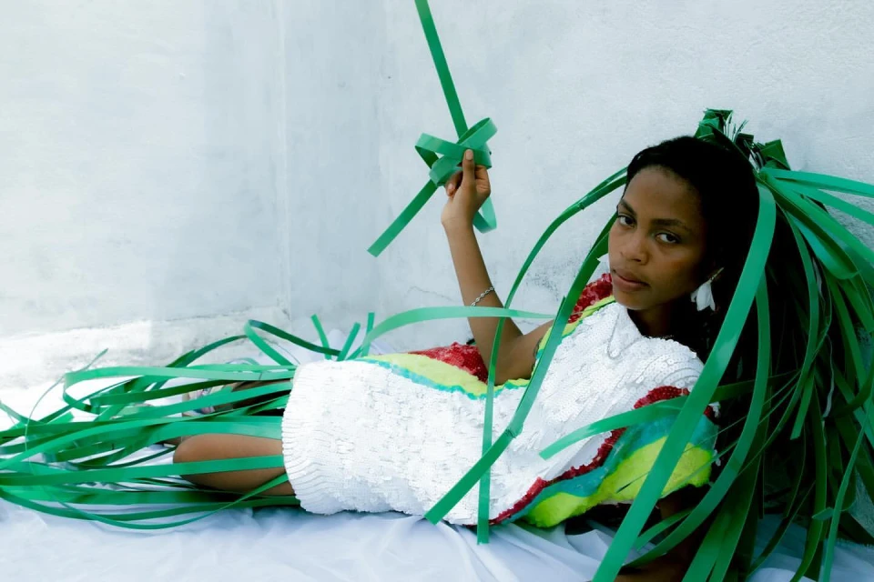 Eye-level shot of an adult woman reclining on a white surface, wearing a colorful dress and surrounded by green cut paper.