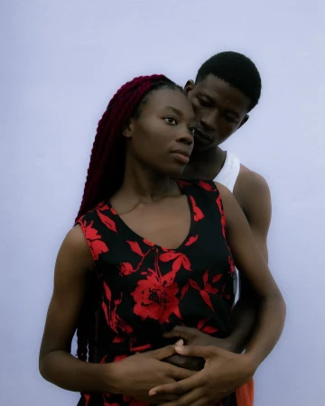 Portrait of a young couple embracing in an intimate pose against a plain backdrop, with the woman in a floral dress as a focal point.