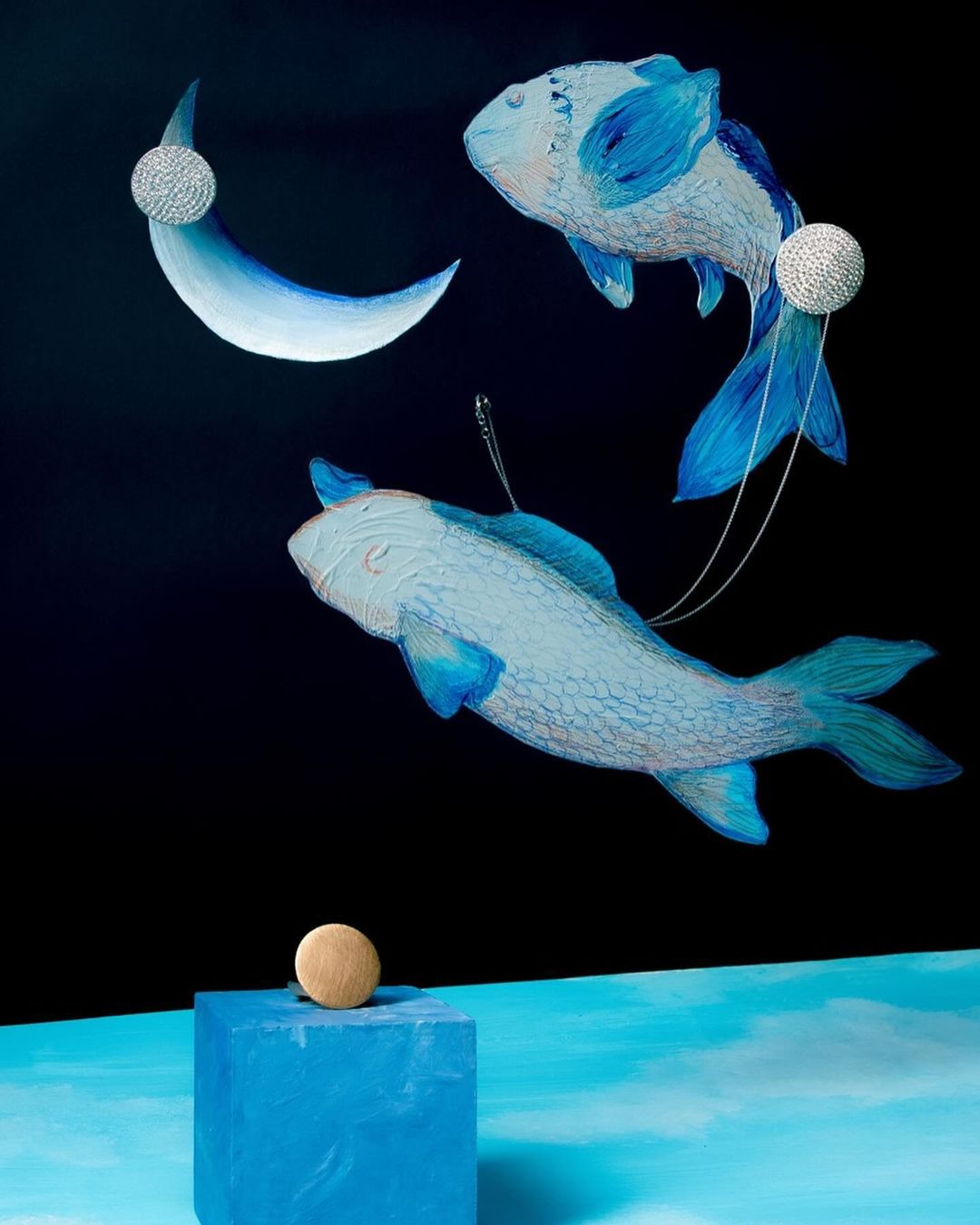 Surreal composition featuring two blue fish swimming against a black background, complemented by a crescent moon and geometric shapes.