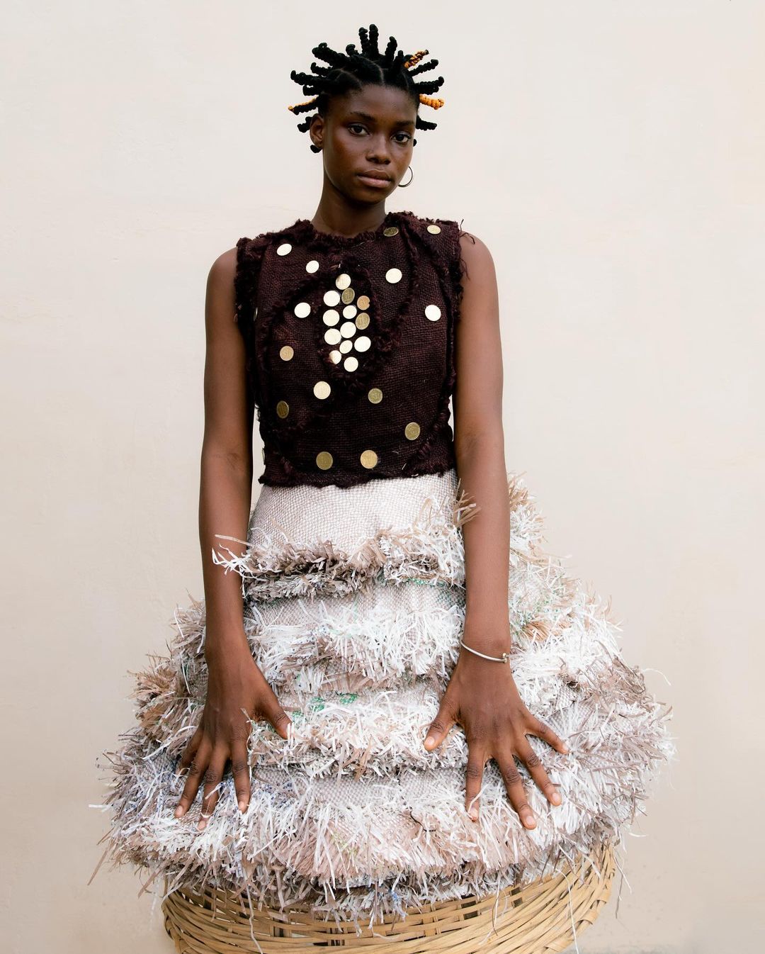Portrait of a Black woman wearing a dark embellished sleeveless top and a heavily textured fringe skirt by Delali Ayivi.
