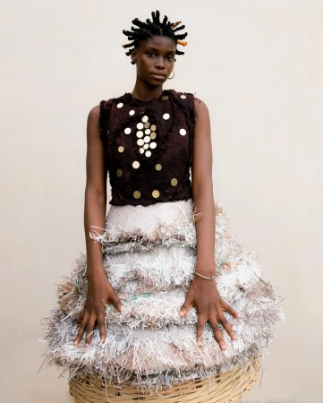 Portrait of a Black woman wearing a dark embellished sleeveless top and a heavily textured fringe skirt by Delali Ayivi.