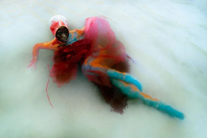 Surreal underwater portrait of a person in colorful clothing, submerged in milky water, creating a dreamy and ethereal atmosphere.