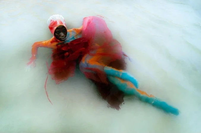 Surreal underwater portrait of a person in colorful clothing, submerged in milky water, creating a dreamy and ethereal atmosphere.