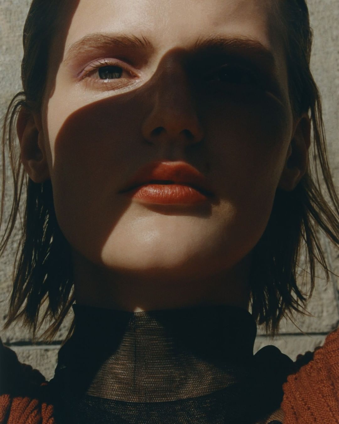 Close-up portrait of a young woman with light skin and brunette hair, featuring dramatic lighting casting shadows across her face.