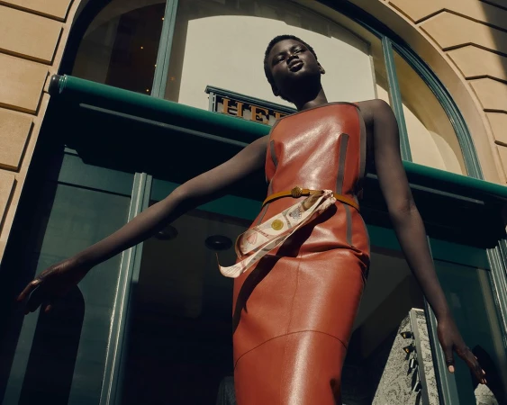 Model in a brown leather dress standing outside a storefront in Paris, captured by Denis Boulze