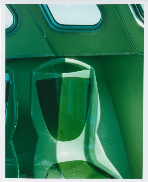 Interior view of a green public transportation vehicle featuring rows of empty seats, overhead windows, and a bright lighting.