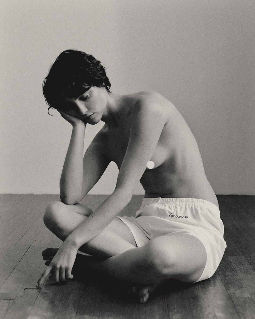 Black and white portrait of a slender woman in a seated pose wearing white shorts, resting her head on her hand in contemplation.