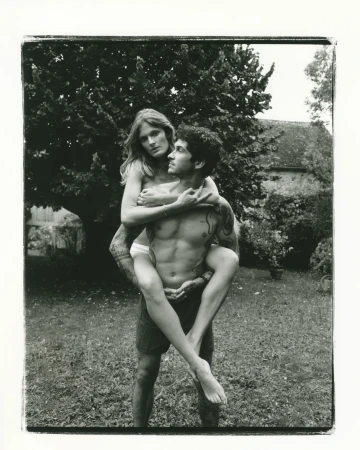 Black and white portrait of a woman being carried on a man back outdoors in a garden by Denis Boulze