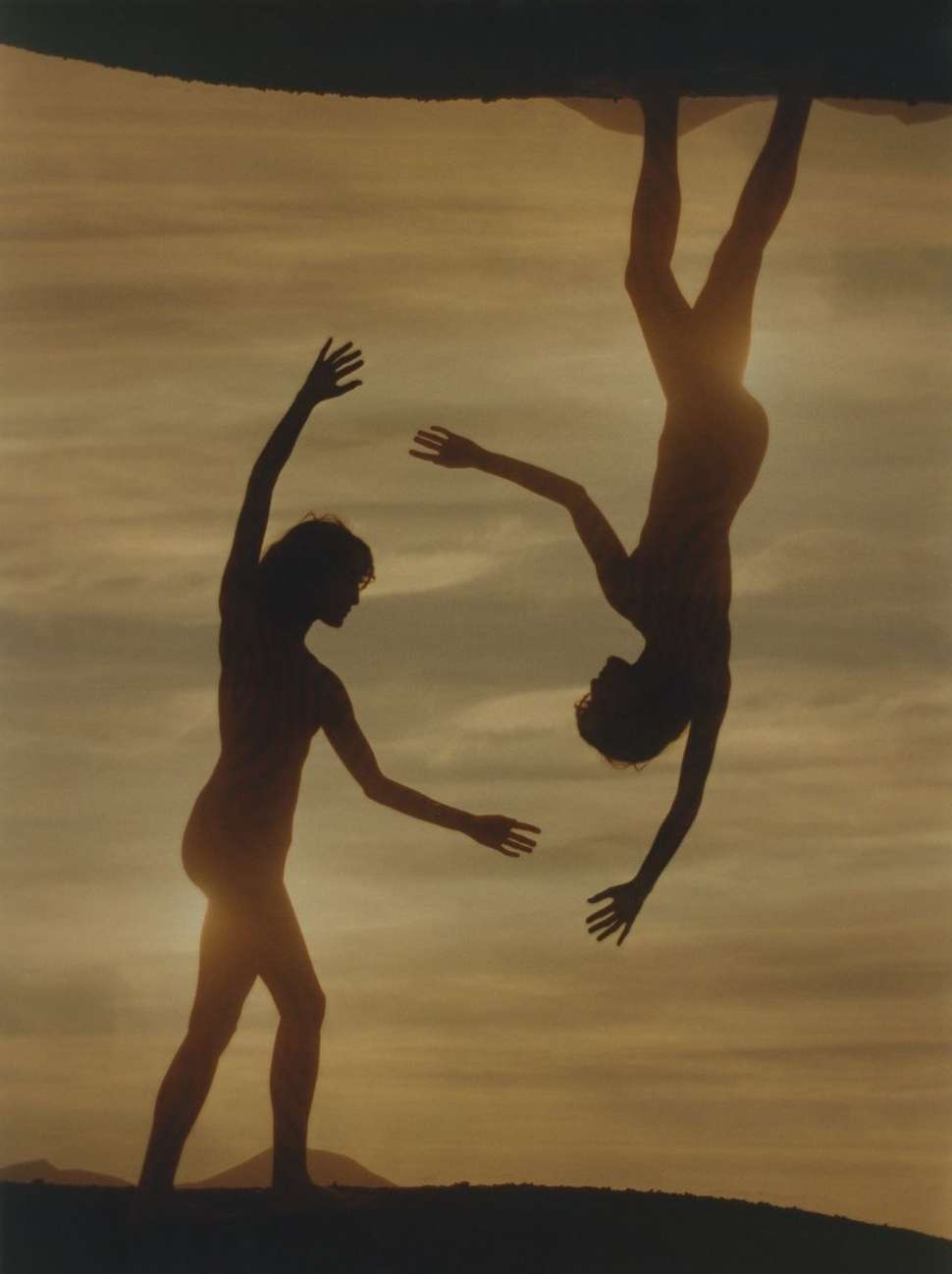 Silhouette of two people against a golden sky, one standing with arms raised, the other inverted in a striking display of movement.
