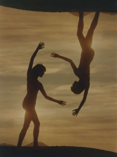 Silhouette of two people against a golden sky, one standing with arms raised, the other inverted in a striking display of movement.