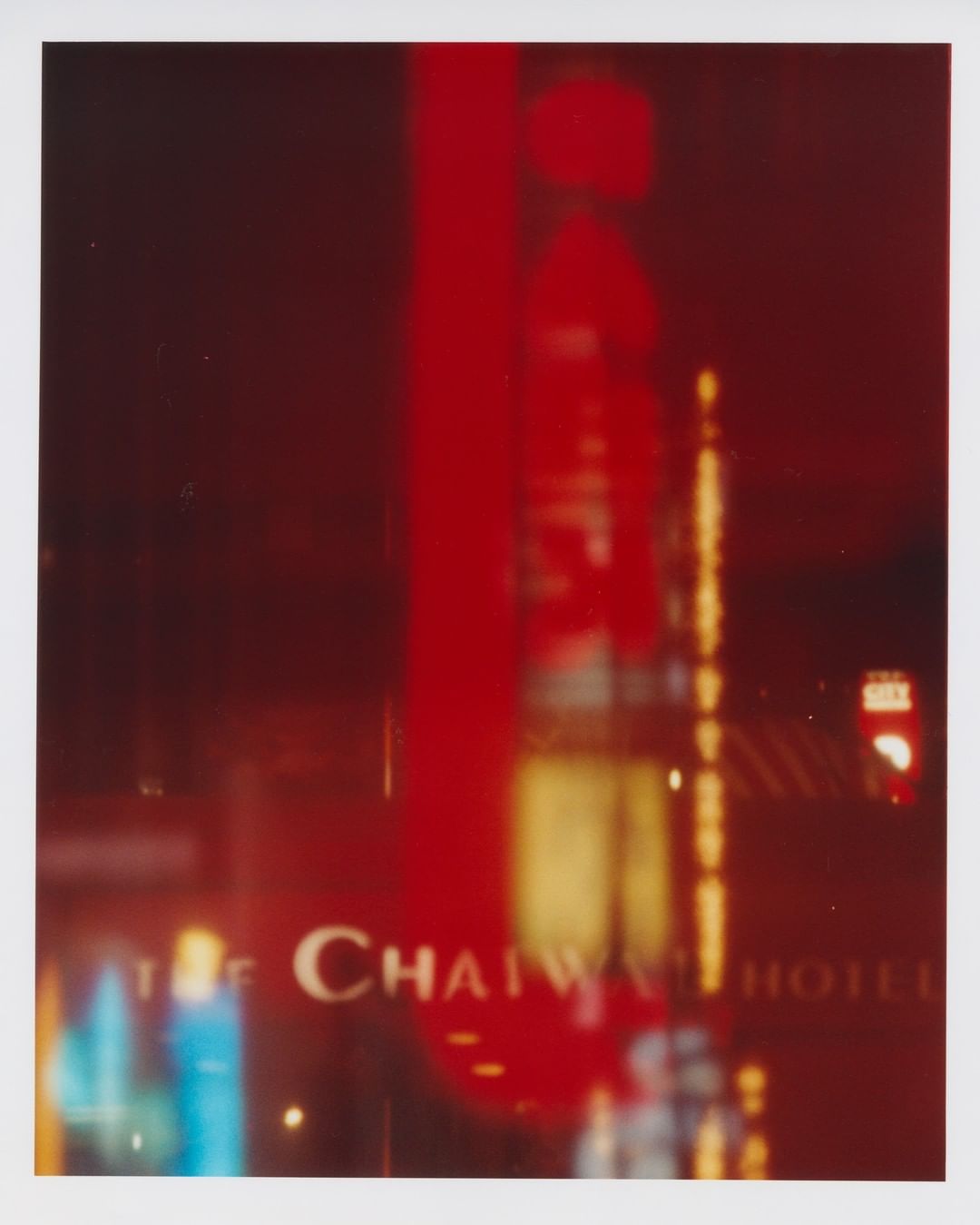 Blurred image of the Chaiwai Hotel at night, with a tall red neon sign and reflections of city lights in the windows. The scene is abstract.